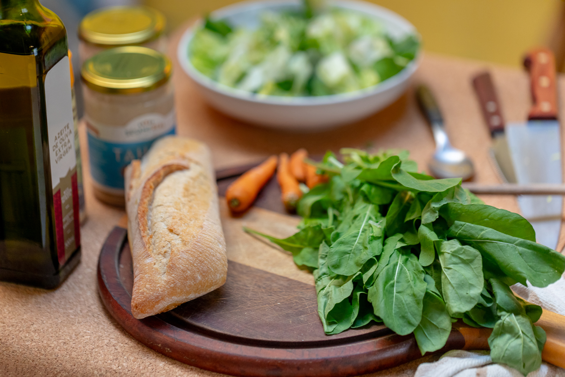 Ingredientes frescos — azeite, pães integrais, folhas verdes e cenouras sobre a bancada